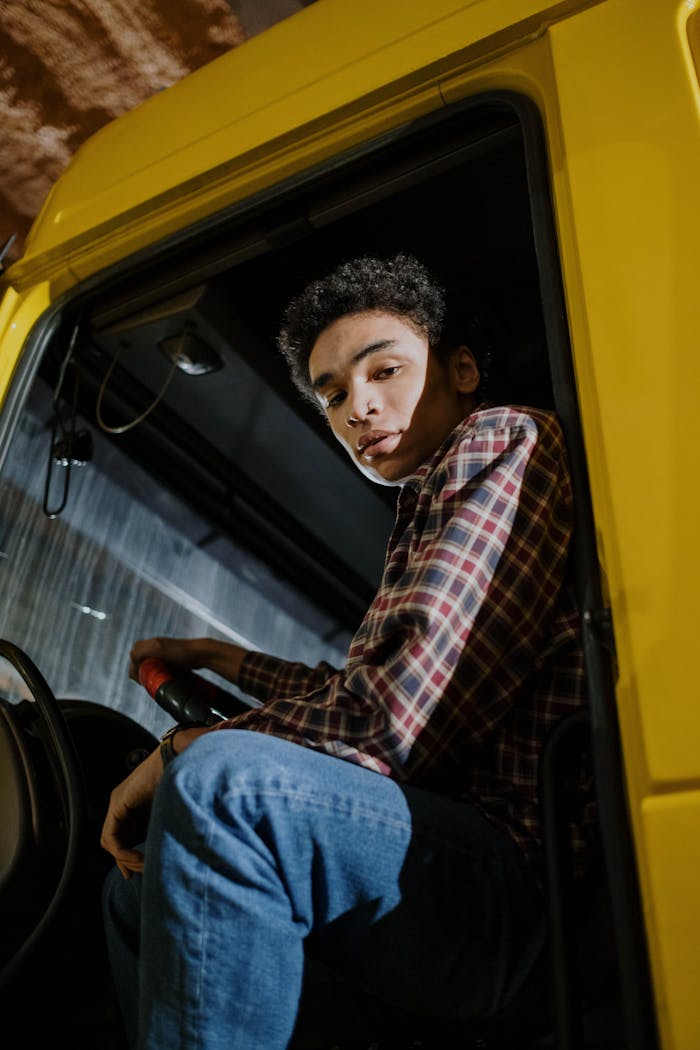 A young man with curly hair seated inside a yellow truck, captured indoors at night.